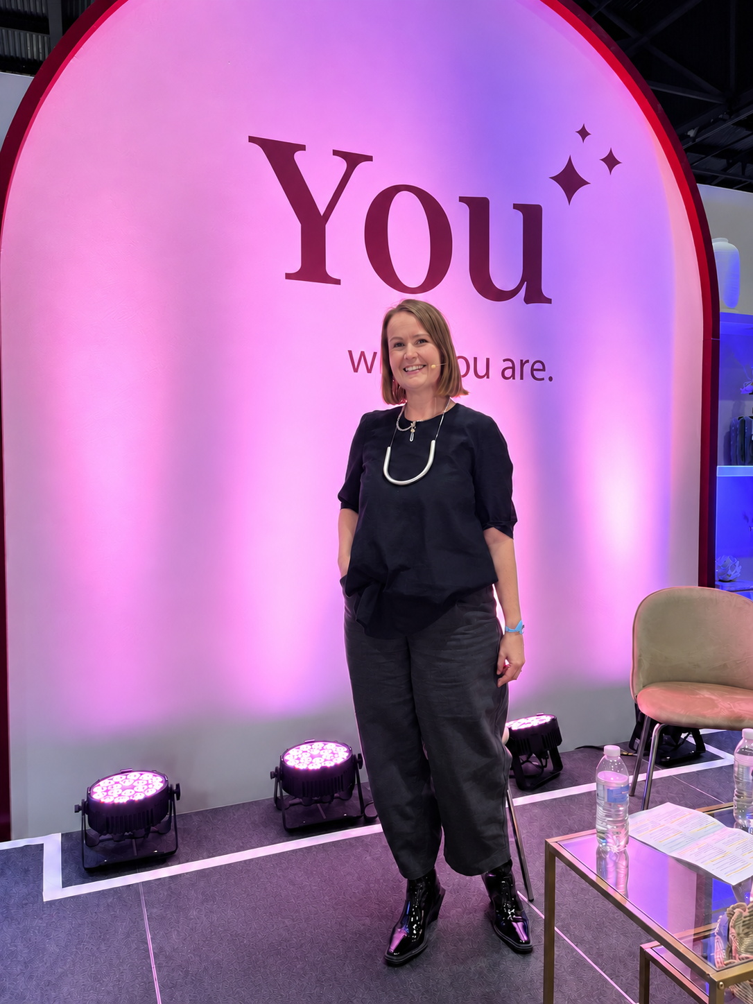 Carly Osman Holme on stage beneath a pink-lit You backdrop